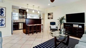 A modern living room with a kitchen, a bar area, a television, and a ceiling fan.