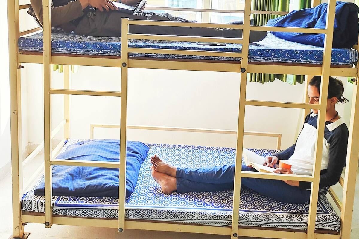 A bunk bed with two levels, a laptop on the top bunk, and a person reading on the bottom bunk.