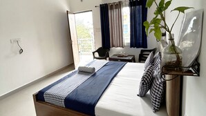 A bedroom with a wooden bed, a small table, a chair, and a potted plant. - UbEx Home Rishikesh - Hostel (Narendranagar)