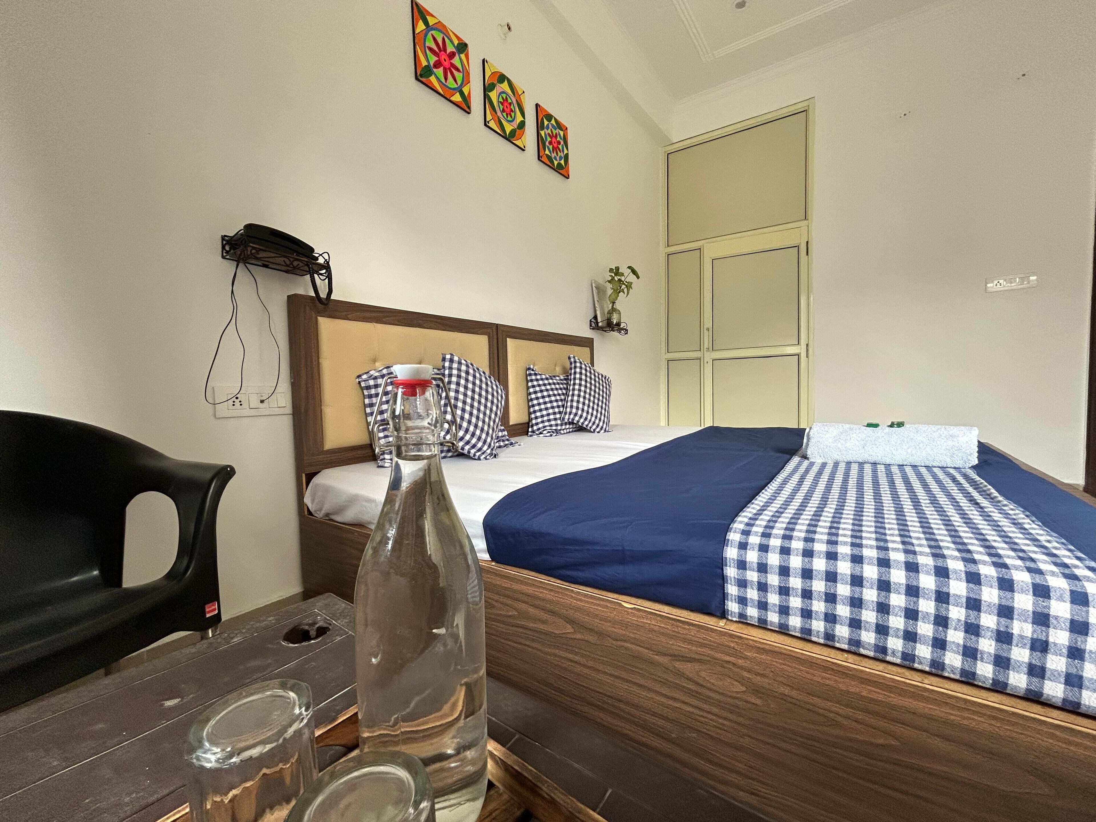 Une chambre d’hôtel avec un lit en bois, une literie à carreaux, une bouteille sur la table et une chaise.