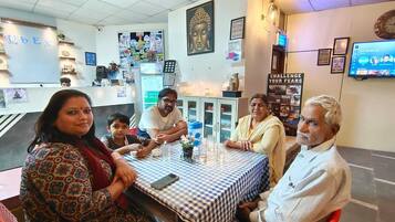 Een restaurant interieur met een geruit tafelkleed, een Boeddha-beeld en een tv aan de muur waarop een menu wordt getoond.