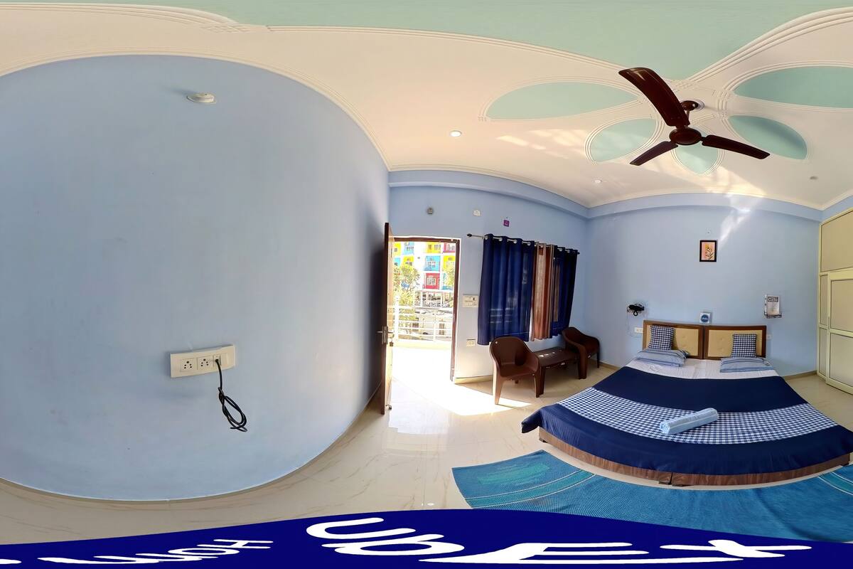 A spacious bedroom with a curved ceiling, a bed with a blue and white checkered bedspread, a ceiling fan, and a view of the outside through a door.