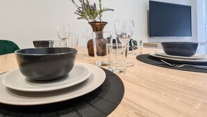 A dining table with a bowl, plates, glasses, and a vase with flowers. - Phaedrus Living: Seaside Luxury Flat Lighthouse 69 (Paphos)