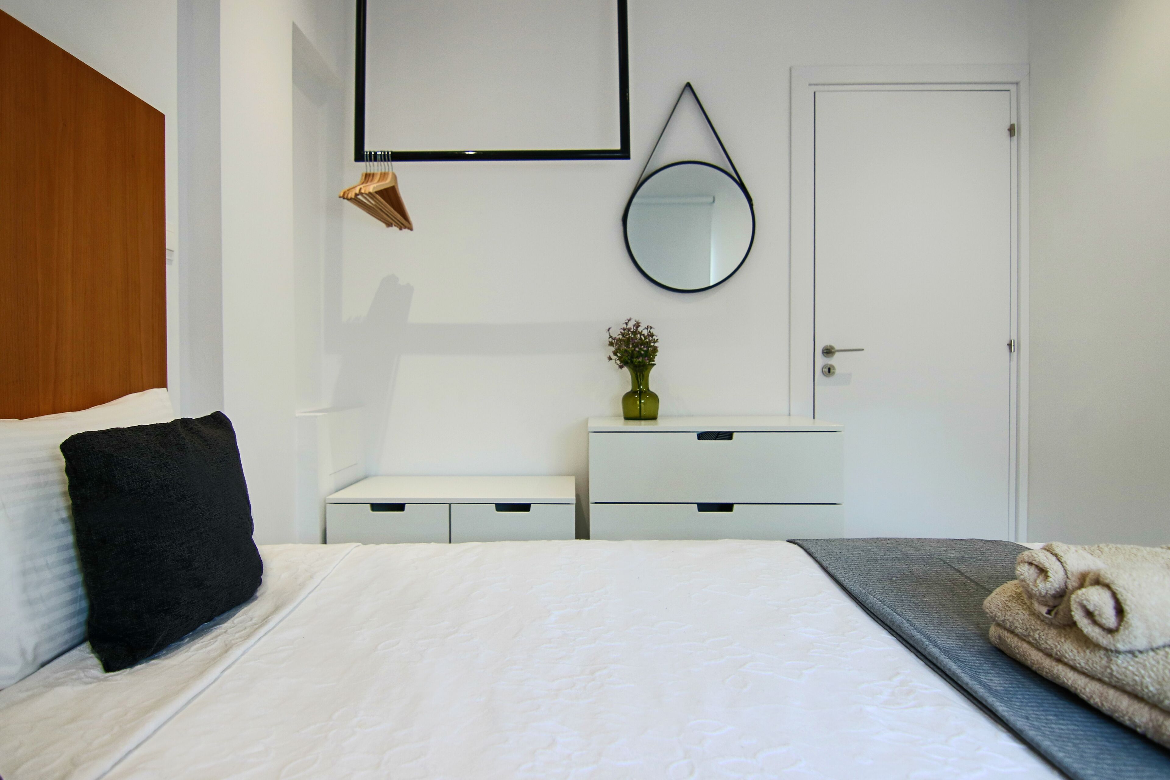 Un dormitorio ordenado con cama, mesita de noche, cómoda, espejo y puerta.