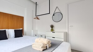 A modern bedroom with a wooden headboard, a bed with white and black bedding, a bedside table with a vase, and a round mirror on the wall. - Phaedrus Living: Seaside Luxury Flat Lighthouse 69 (Paphos)