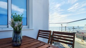 A balcony with a wooden table and chairs, a vase with flowers, and a view of the sea and boats. - Phaedrus Living: Seaside Luxury Flat Lighthouse 69 (Paphos)