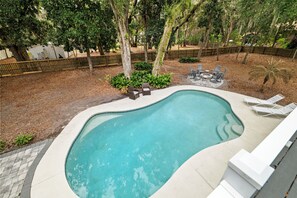 Une piscine à bord incurvé, entourée d’une terrasse en bois et d’une clôture.