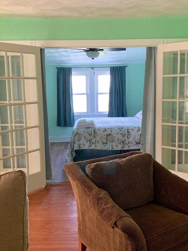 Una stanza con un letto, una ventola a soffitto e vista su un'altra camera da letto attraverso una porta aperta.