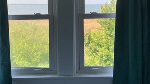 A room with two windows overlooking a body of water and greenery. - Manor and Mutts #2 - Beach Front, Pet Friendly, Wi-Fi, Parking, W/D, King Bed (Norfolk)