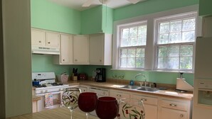 A kitchen with white cabinets, a stove, a sink, and a window with a view of greenery. - Manor and Mutts #2 - Beach Front, Pet Friendly, Wi-Fi, Parking, W/D, King Bed (Norfolk)