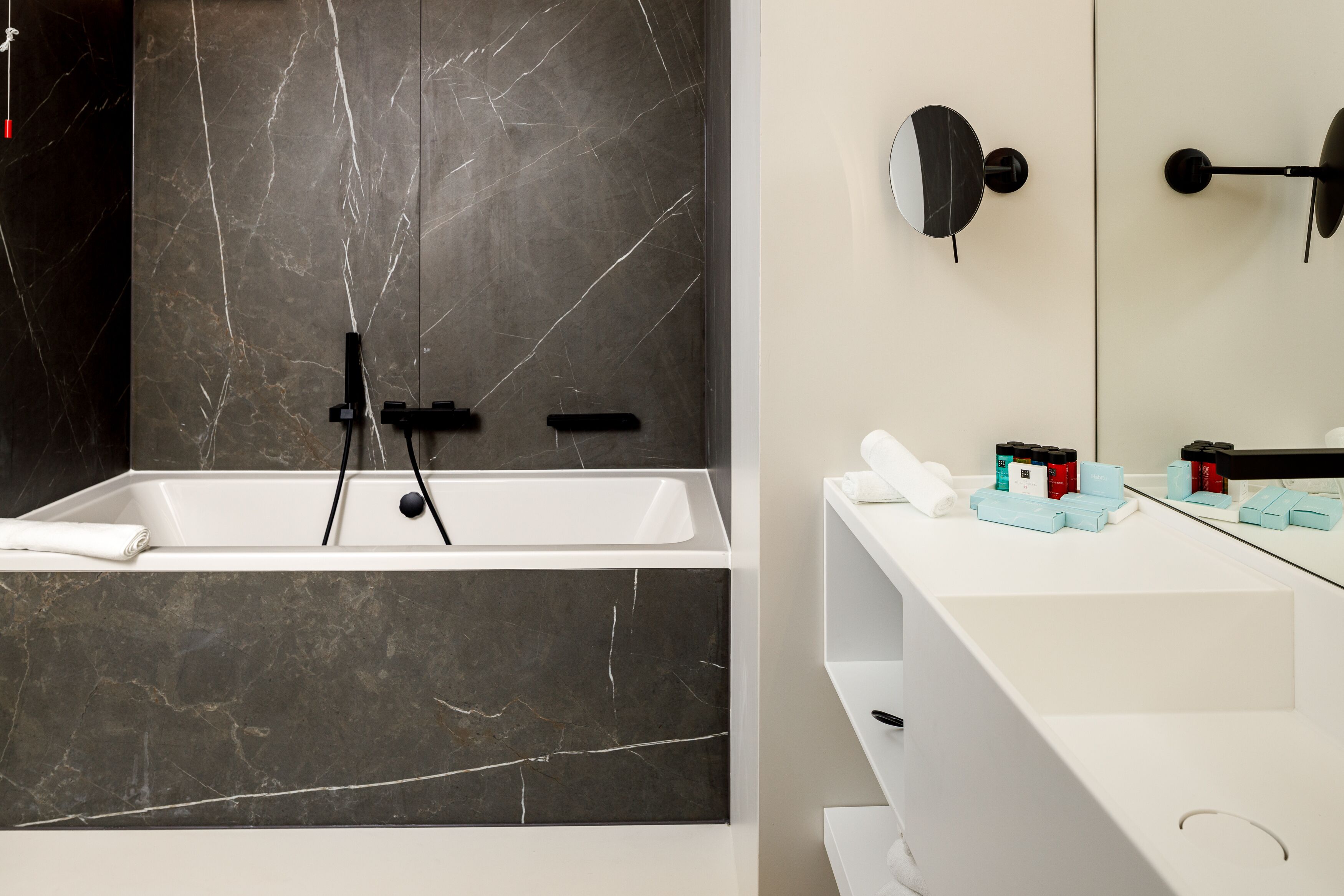 A modern bathroom with a marble sink, a large mirror, and a white bathtub.