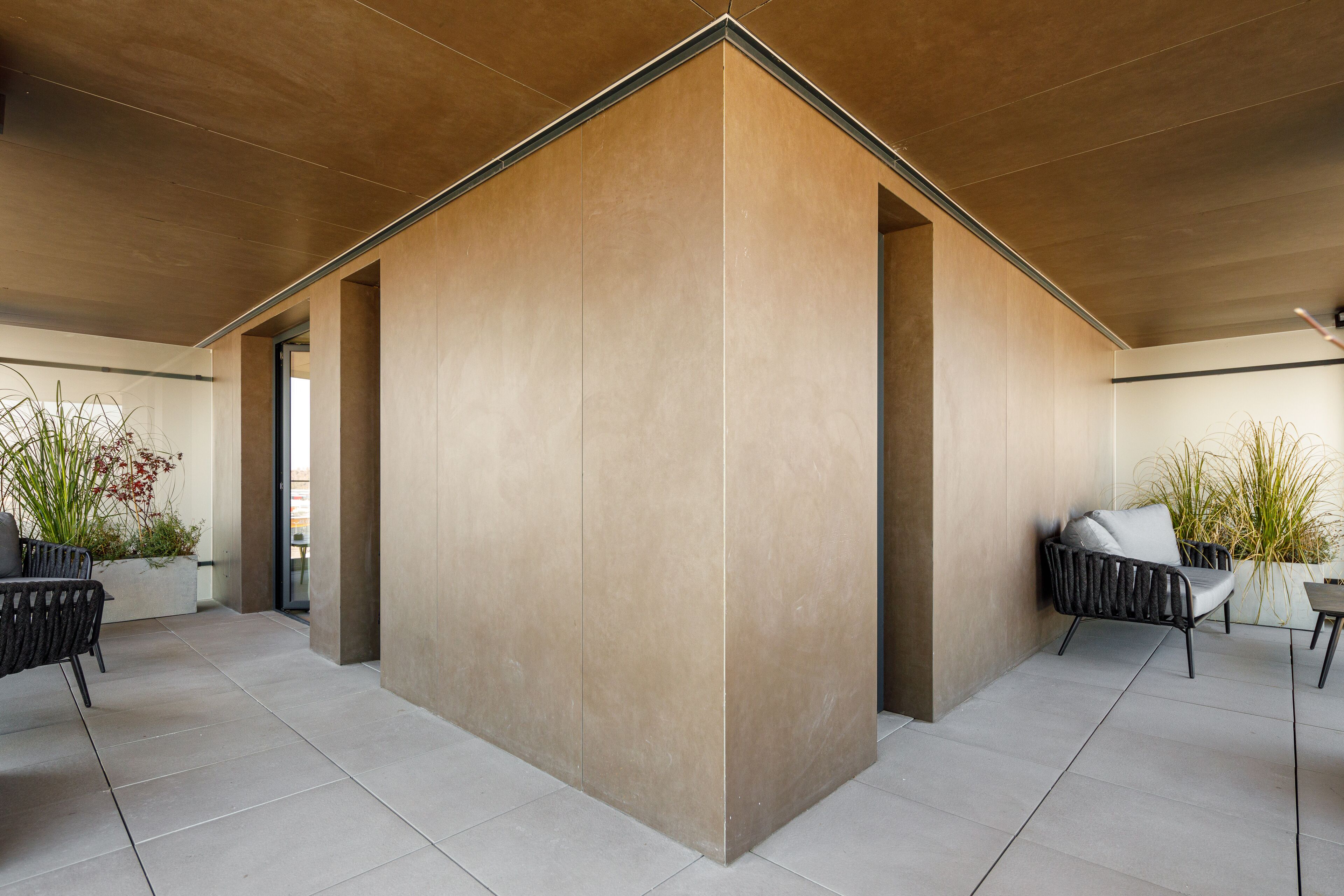 A modern interior with a large central column, tiled flooring, and two seating areas with plants.