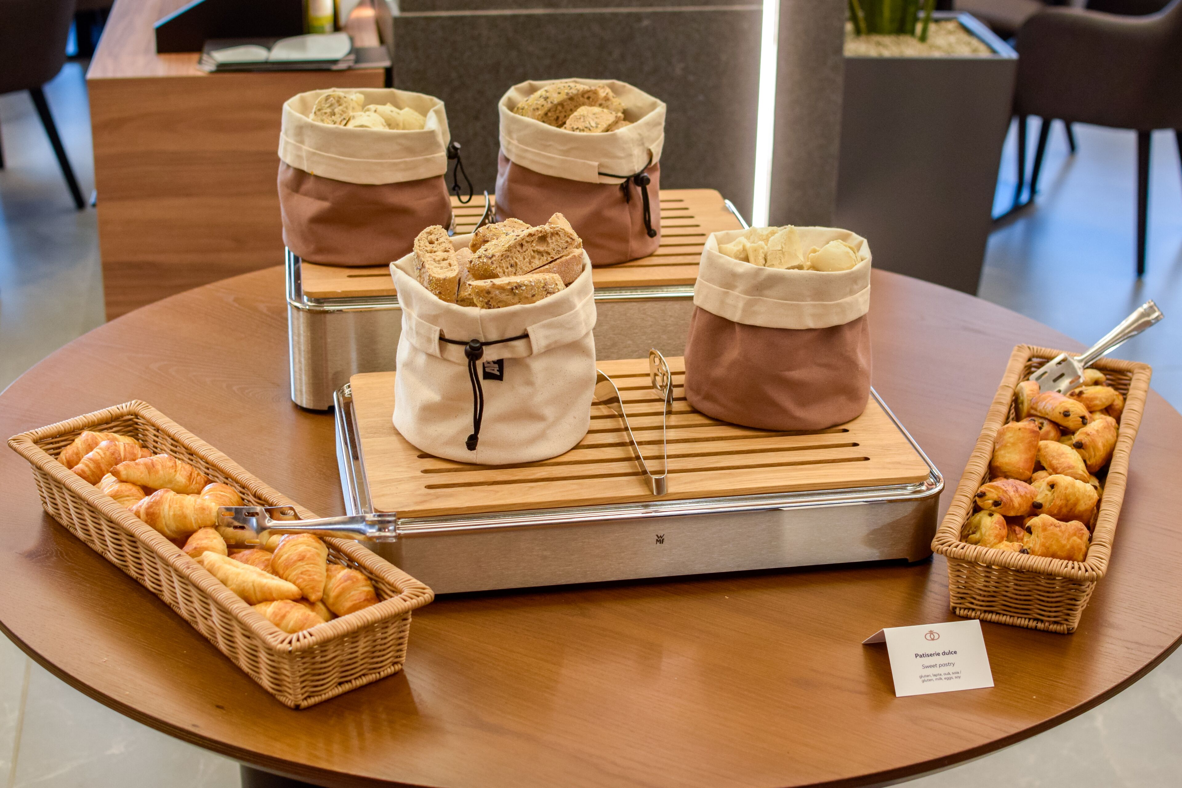Un bufé de desayuno con croissants, bagels y bollería sobre una mesa de madera.