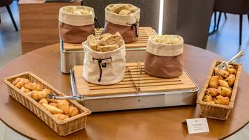 Un bufé de desayuno con croissants, bagels y bollería sobre una mesa de madera.