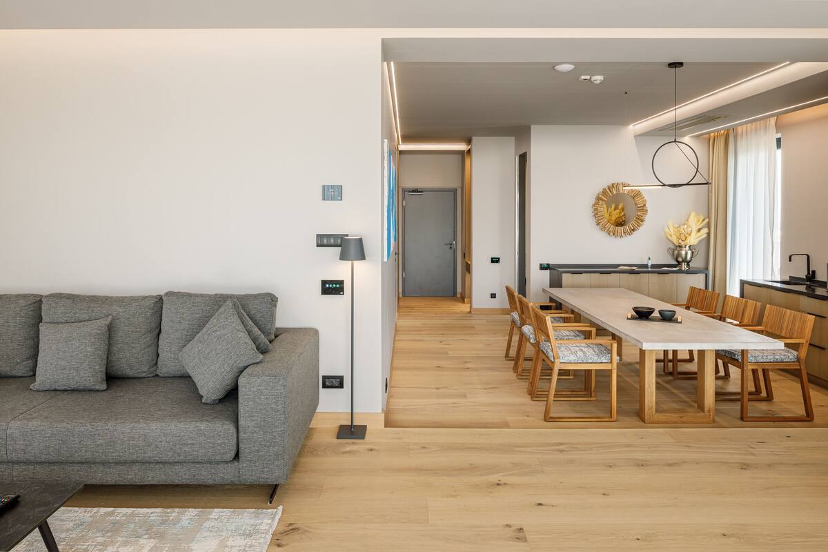 A modern living room with a grey sofa, wooden dining table, and chairs.