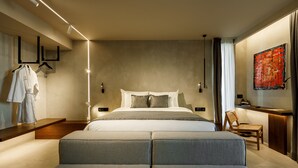A modern hotel room with a large bed, a seating area, a desk, and a painting on the wall. - Qosmo Brasov Hotel (Brasov)