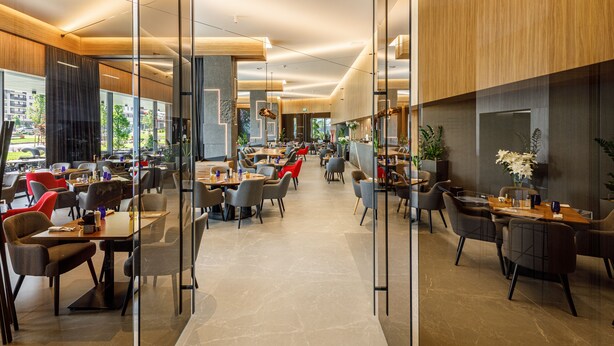 A modern restaurant with glass partitions, wooden accents, and a variety of seating options. - Qosmo Brasov Hotel (Brasov)