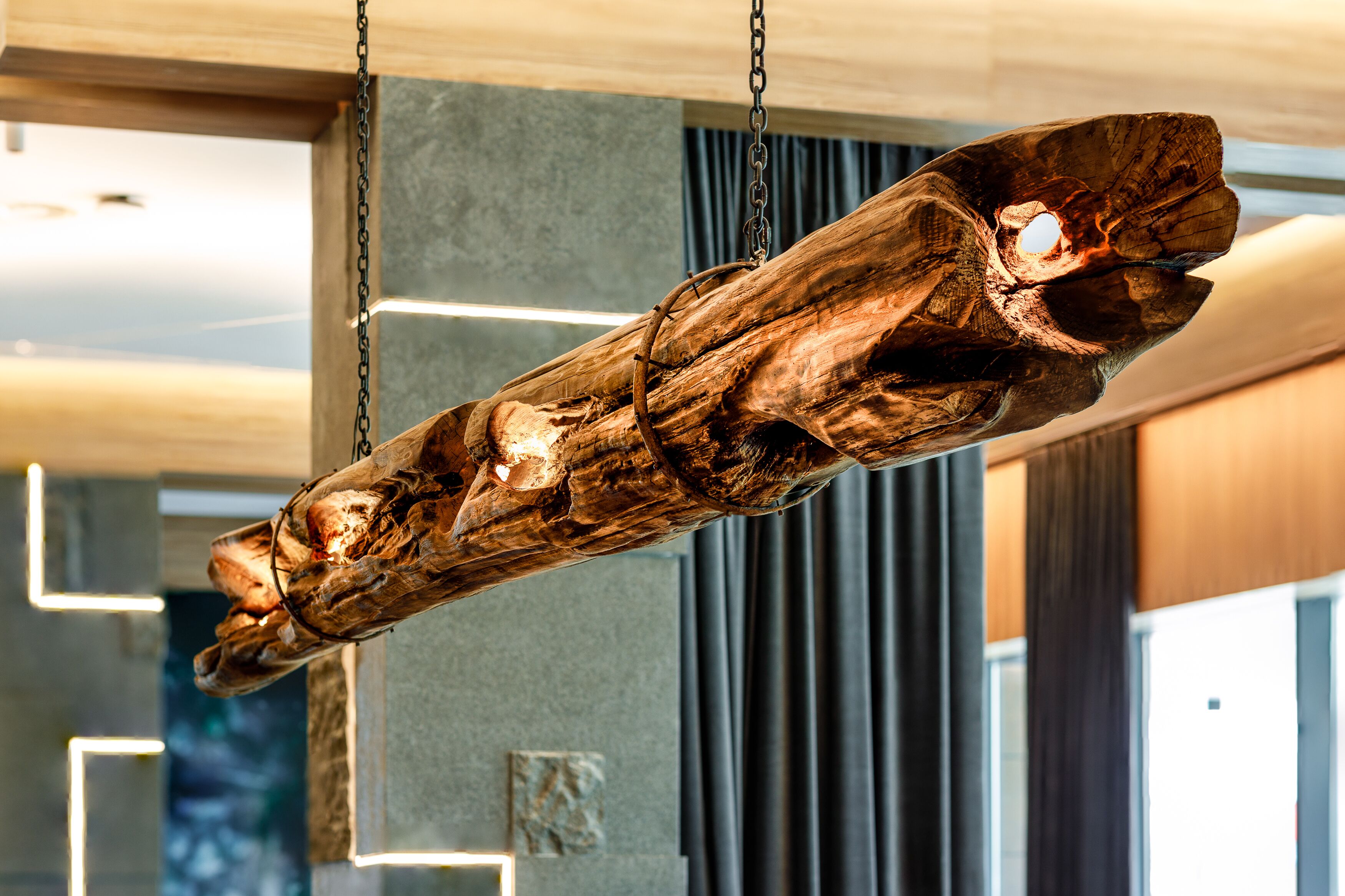 A wooden sculpture suspended from the ceiling in a modern interior space.