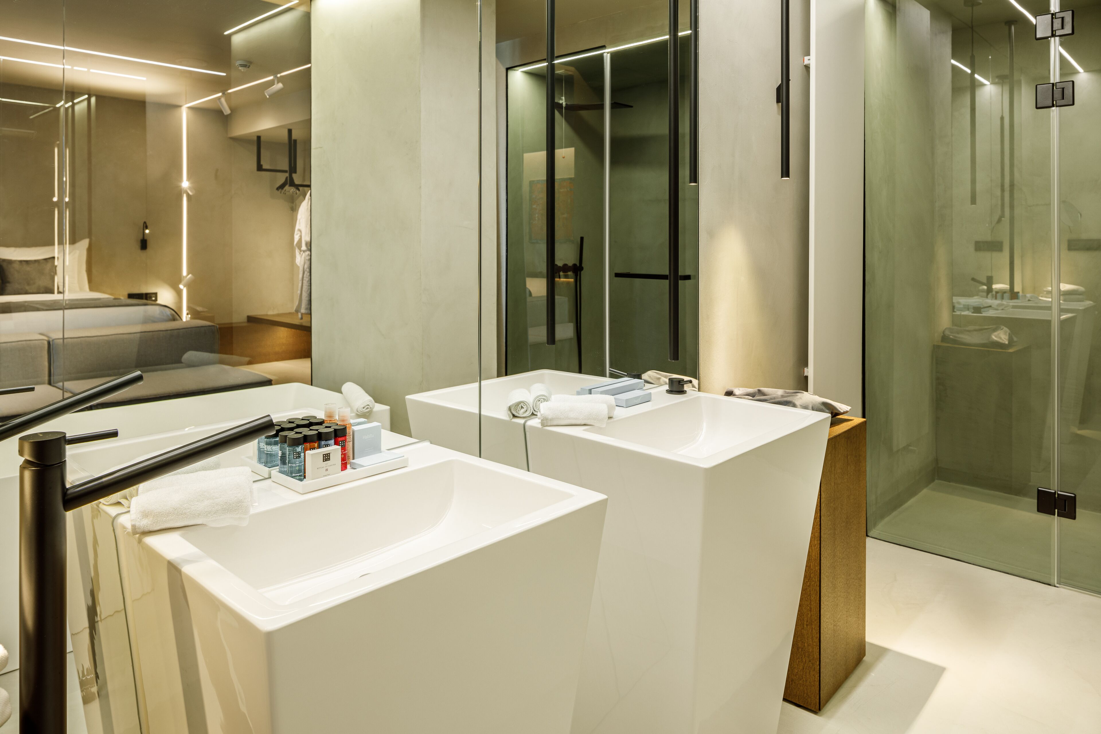 Un baño moderno con dos lavamanos blancos, una cabina de ducha de vidrio y un mueble de tocador de madera.