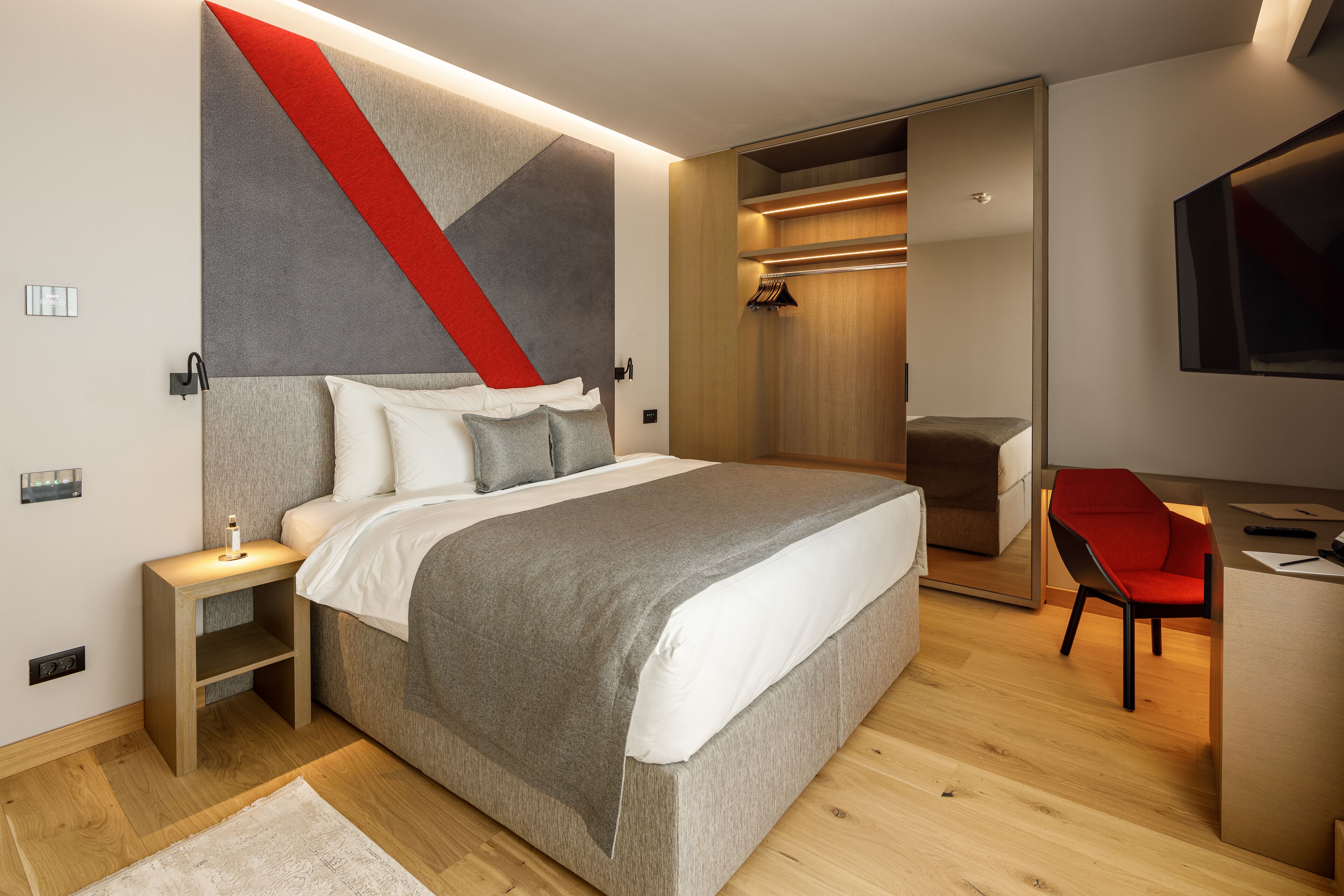 Een moderne slaapkamer met een bed, nachtkastje en een rode stoel.