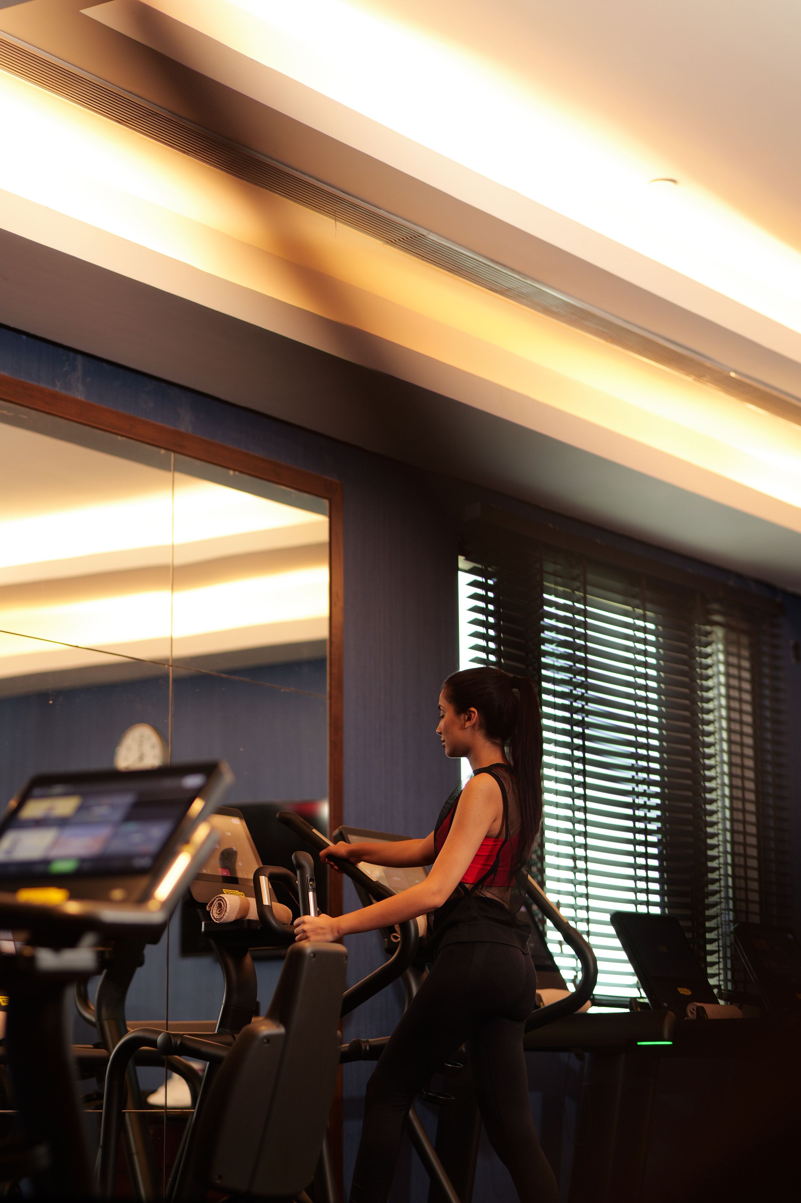 A person using a stationary bike in a gym with a large mirror and windows.
