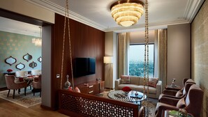 Habitación de hotel moderna con una tele grande, un sofá, zona de comedor y vistas a la ciudad.