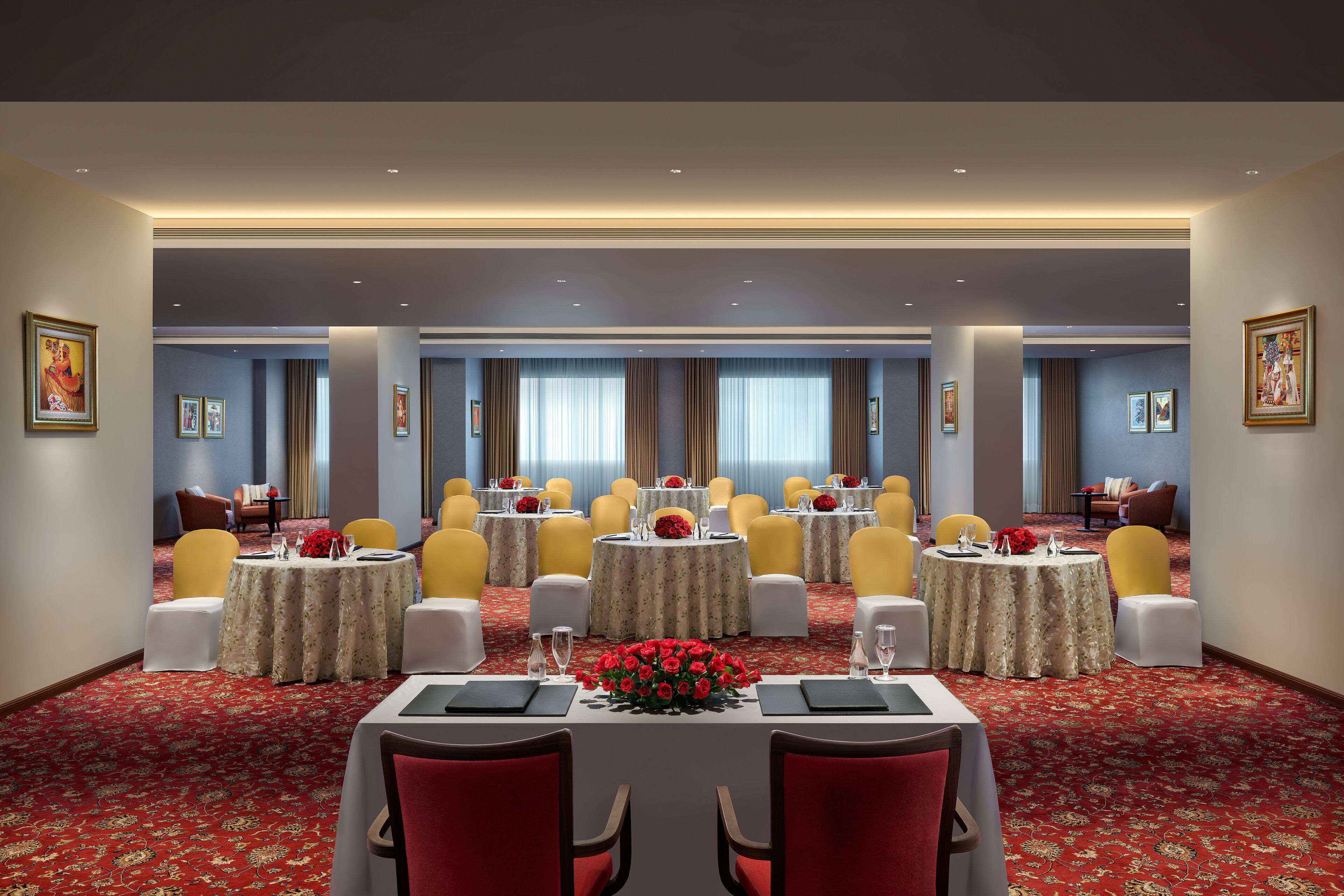 A conference room with round tables, yellow chairs, and red floral centerpieces.