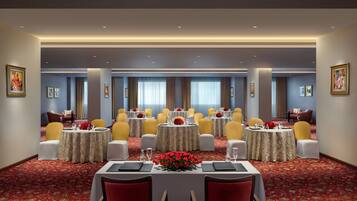 A conference room with round tables, yellow chairs, and red floral centerpieces.