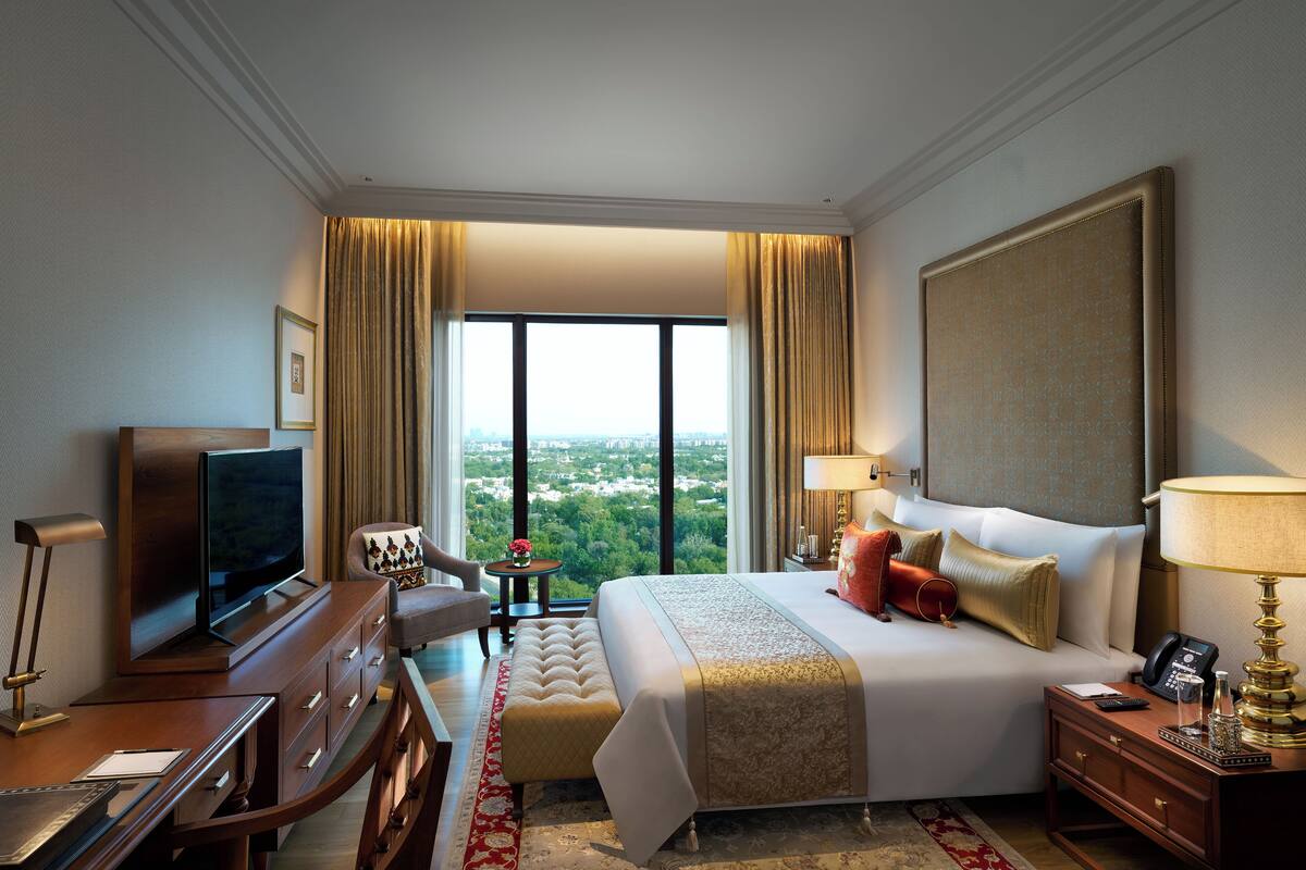 Ein Hotelzimmer mit einem großen Bett, einem Fernseher, einem Schreibtisch und Blick auf die Stadt.