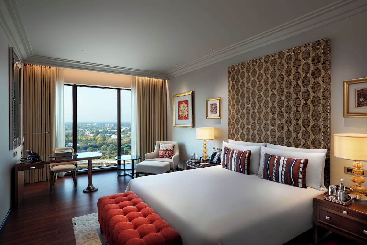 Ein Hotelzimmer mit einem großen Bett, einem Schreibtisch, einem Stuhl, einem roten Hocker und Blick auf die Stadt.