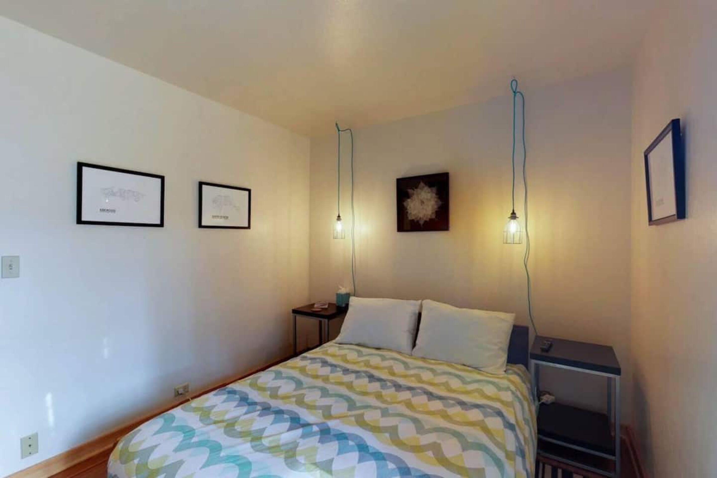 A bedroom with a bed, bedside tables, and wall-mounted lights.
