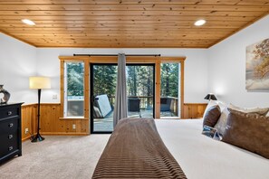 A bedroom with a bed, a dresser, a lamp, a painting, and a sliding glass door leading to an outdoor deck. - Black Bear by AvantStay | Spacious Lodge in Tahoe Donner w/ Game Room & Hot Tub (Truckee)