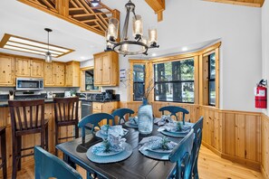 A modern kitchen with wooden cabinets, a dining area with blue chairs, and a large window. - Black Bear by AvantStay | Spacious Lodge in Tahoe Donner w/ Game Room & Hot Tub (Truckee)