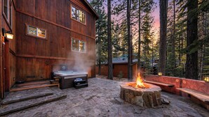 Eine Holzblockhütte mit einer Steinterrasse, einem Whirlpool und einer Feuerstelle.