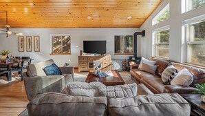 Ein geräumiges Wohnzimmer mit Holzbalkendecke, Ledersofas, einem Couchtisch und einem Fernseher.