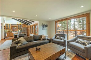 Relax in a spacious living area with a sectional sofa and armchairs, surrounded by forest views.