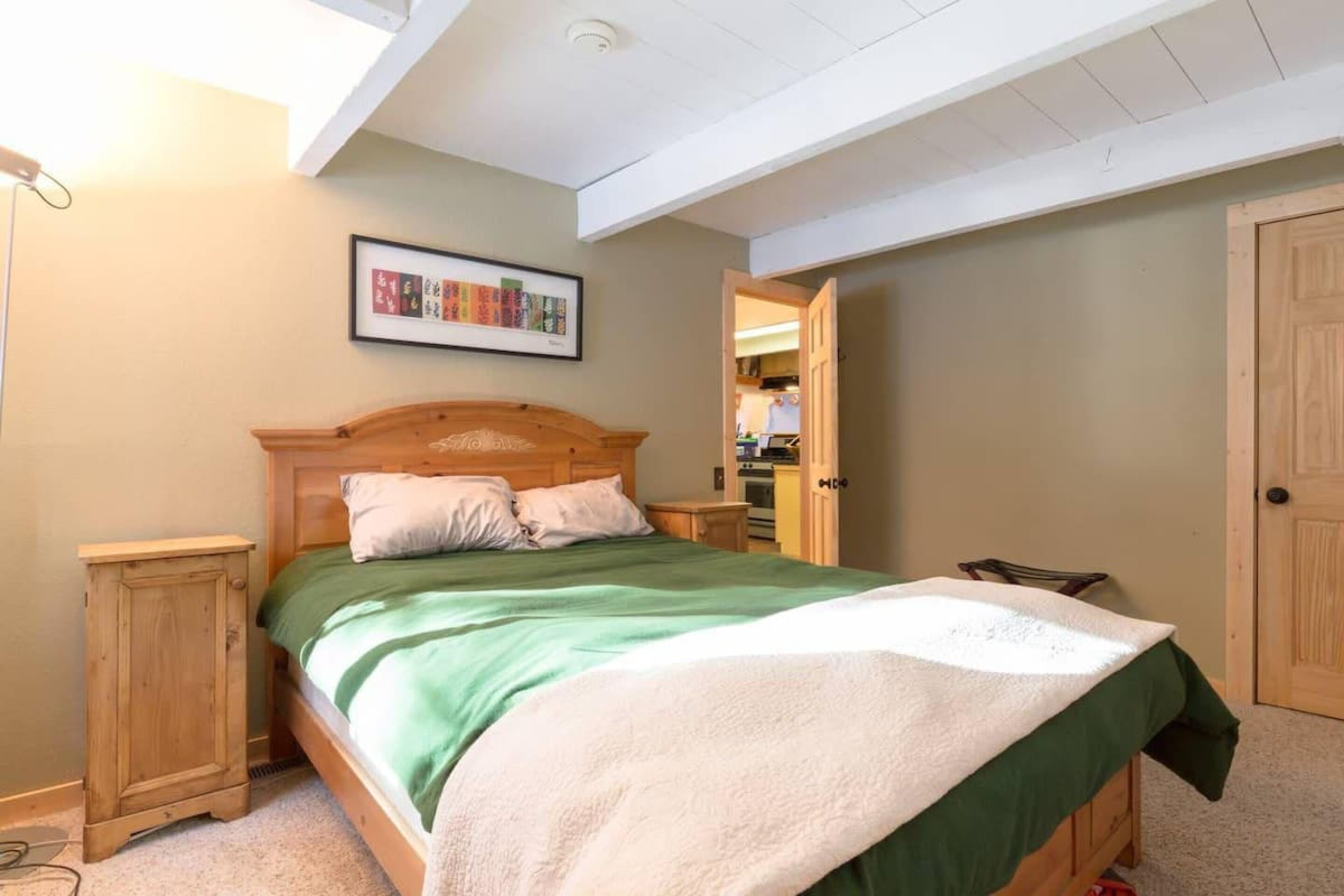 Camera da letto con un letto in legno, biancheria verde e bianca, un armadio in legno e una lampada a soffitto.