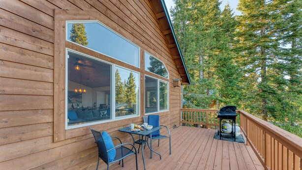 Una cabaña de madera con terraza, ventanas amplias y una parrilla.