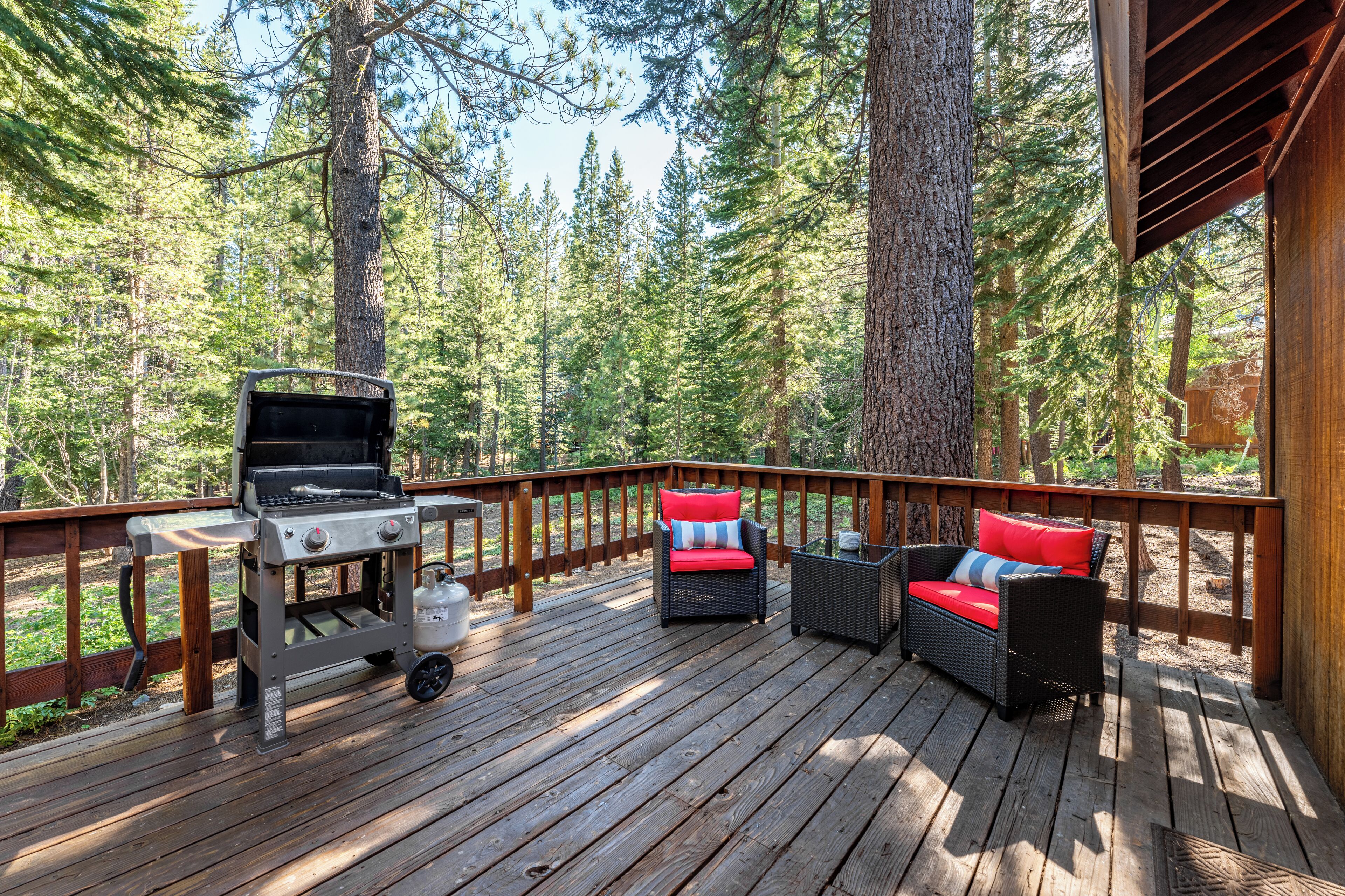 Una terraza con una parrilla, muebles de mimbre y vista a un bosque.