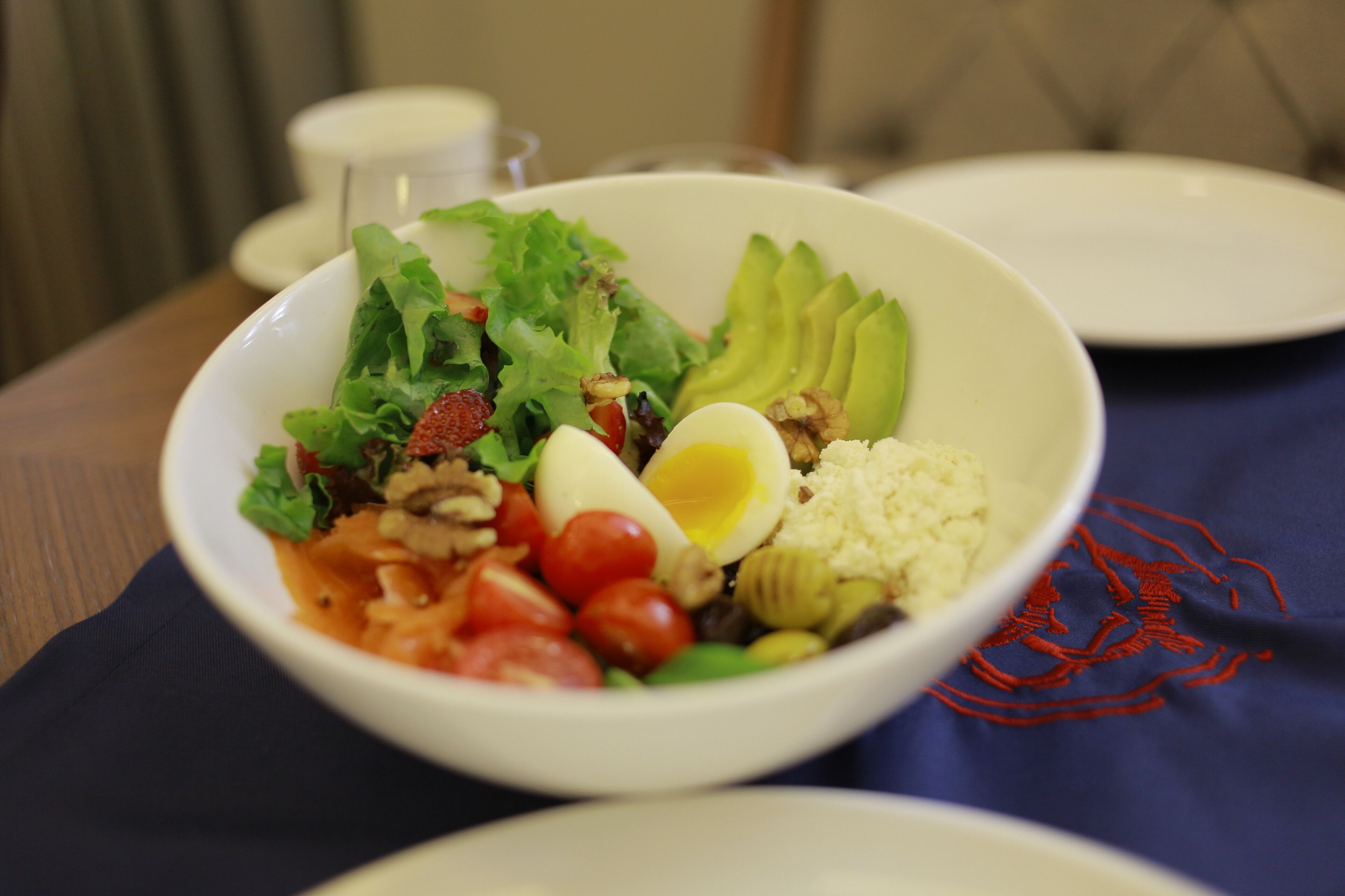 A bowl of salad with various ingredients including lettuce, tomatoes, avocado, and a boiled egg.