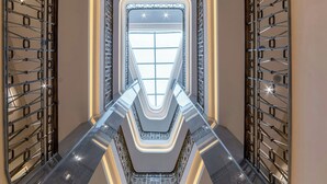 A modern interior with a central glass elevator shaft, metallic railings, and a geometric floor design. - Orientbank Hotel Istanbul, Autograph Collection (Istanbul)