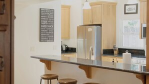 A modern kitchen with a central island, bar stools, wooden cabinets, and a refrigerator.