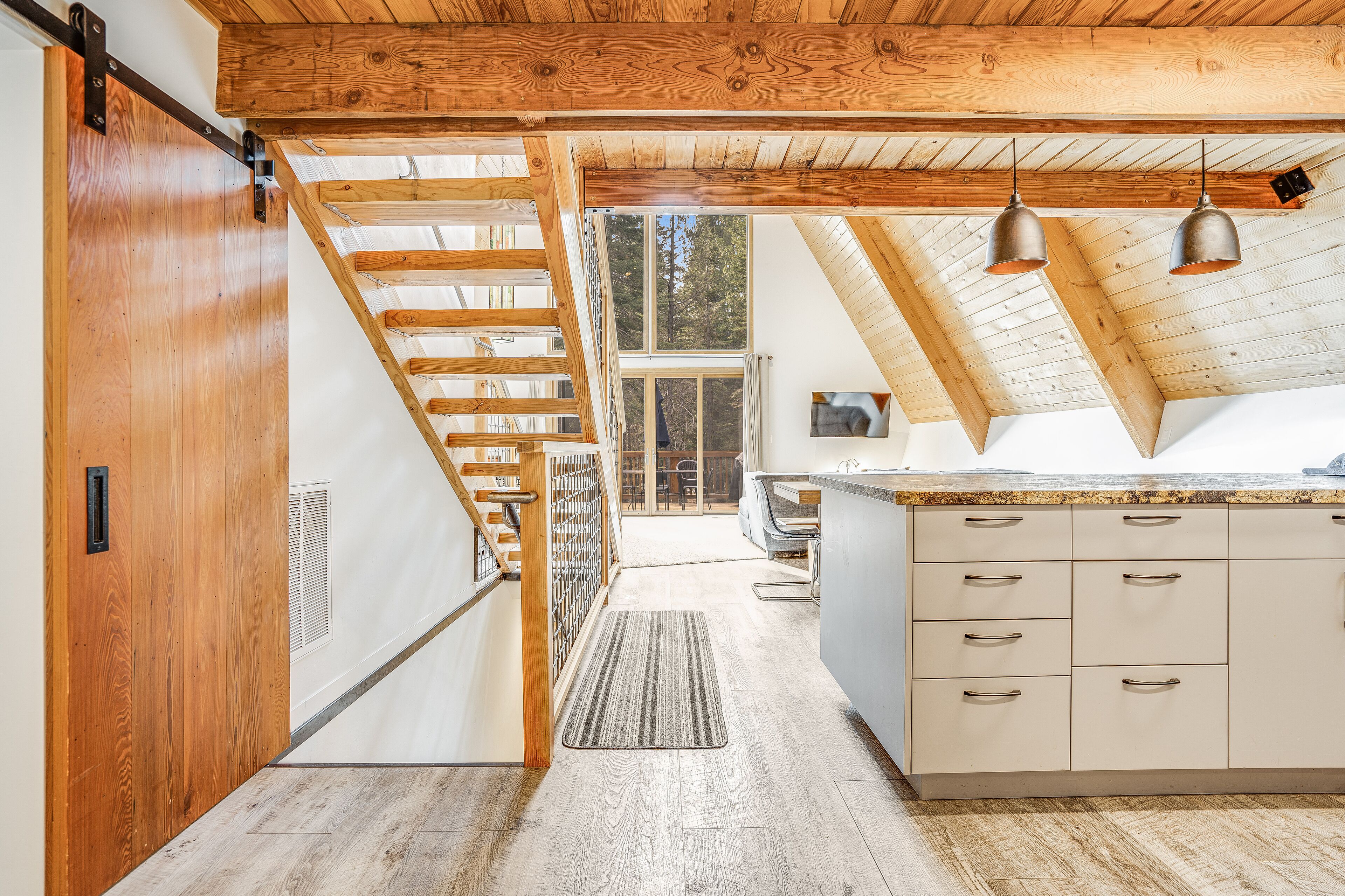 Una cucina moderna con soffitto in legno, isola con pensili e vista su una zona pranzo tramite una porta in vetro.