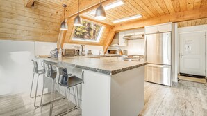 A kitchen with a large island, bar stools, a stainless steel refrigerator, and a skylight.