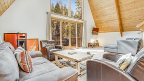 A spacious living room with a high ceiling, large windows, and a view of trees.