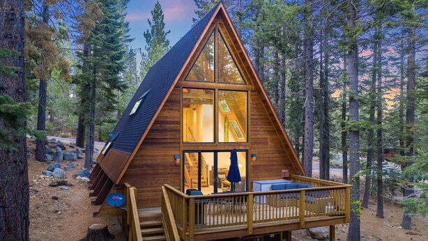 A wooden cabin with a balcony, a staircase, and a view of the surrounding forest.
