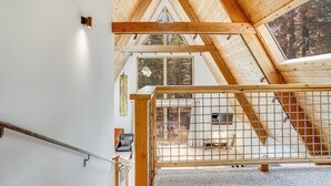 A high-ceilinged room with wooden beams, a large window, and a view of the outdoors.