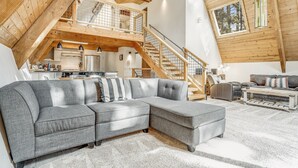 A spacious loft with a large gray sectional sofa, a wooden staircase, and a kitchen area.
