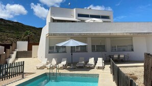 A modern two-story building with a swimming pool, white exterior, and a view of a hilly landscape. - Wonderful modern, spacious and comfortable villa (Fornells)