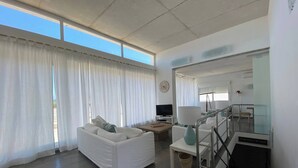 A spacious living room with a white sofa, a television, and a lamp. There is a staircase leading to an upper level. - Wonderful modern, spacious and comfortable villa (Fornells)
